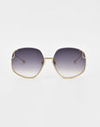 A pair of luxurious For Art's Sake® Drape sunglasses with gold frames and large, slightly hexagonal lenses. The lenses have a gradient tint, transitioning from dark at the top to lighter at the bottom. The frame features intricate metal detailing on thin arms and a minimalistic design. The background is plain white.
