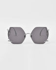 A pair of stylish, rimless, hexagon-shaped sunglasses with dark tinted lenses and thin metal arms. These limited edition Cry Me a River sunglasses by For Art's Sake® stand out against the white background, highlighting their sleek design and modern aesthetic.