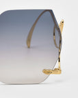 Close-up of For Art’s Sake® Cry Me a River limited edition sunglasses with large hexagonal gradient lenses, gold metal frames, and decorative gold hinges, set on a plain white background.