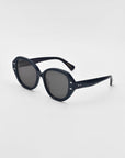 Mirage White by For Art's Sake® are oval sunglasses with thick, plant-based acetate frames, dark lenses, and small metallic accents by the hinges. Slightly curved arms add comfort, combining style and sustainability in an eco-friendly design.