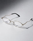 A pair of elegant, modern Thorn oval glasses by For Art's Sake® featuring thin metal frames and black temple tips rest on a light grey surface, with "FOR ARTS SAKE" printed on the left lens—true statement eyewear for any occasion.