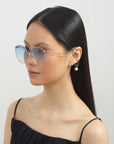 Woman with straight black hair wears For Art's Sake® Birthday Cake-Blue large round sunglasses with blue lenses, a black sleeveless top, and unique faux pearl earrings, posing against a plain light background.