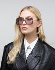 A person with long blonde hair dons For Art's Sake® Icon-ARC large handmade acetate sunglasses, a white collared shirt, and a black textured leather jacket. The neutral background accentuates their stylish look, while the D-frame shades offer full UVA & UVB protection.
