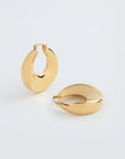 A pair of shiny, 18kt gold-plated Moon Earrings Gold by For Art's Sake® are displayed against a plain, light background. The earrings boast a chunky oval design and have a slight curve, enhancing their modern and elegant appearance. One earring stands upright, while the other lies flat.