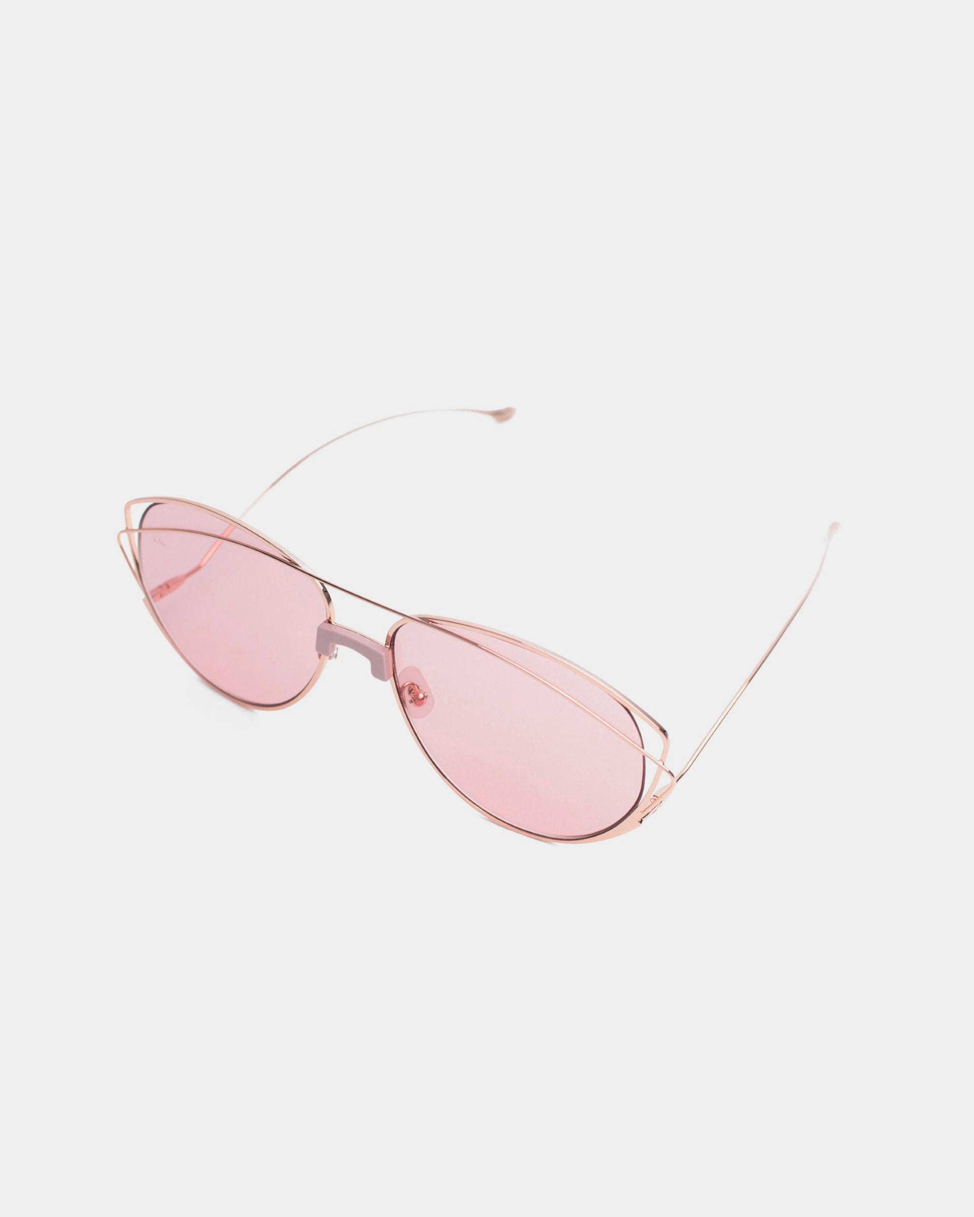 A pair of Dark Eyes sunglasses from For Art's Sake®, featuring thin, stainless steel frames and pink-tinted nylon lenses, resting on a white background. The frame design is minimalist with no visible embellishments, offering 100% UV protection and giving the sunglasses a sleek, modern look.