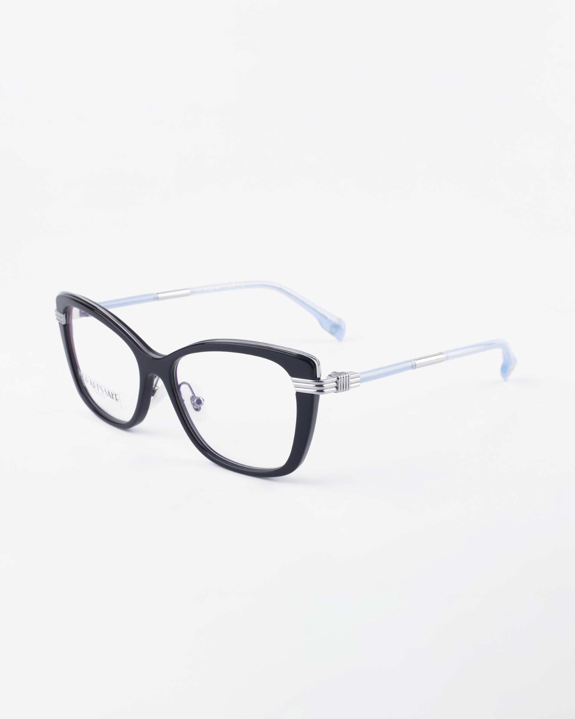 The Amour by For Art's Sake® features black cat-eye frames with clear lenses, silver hinge details, and light blue temples. Adjustable nose pads offer all-day comfort. Shown on a white background for an elegant display.
