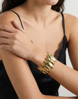 A woman in a black lace-trimmed camisole rests her hand on her arm, showcasing The Forms Bangle by For Art's Sake®—a modern gold accessory with an organic, sculpted design.