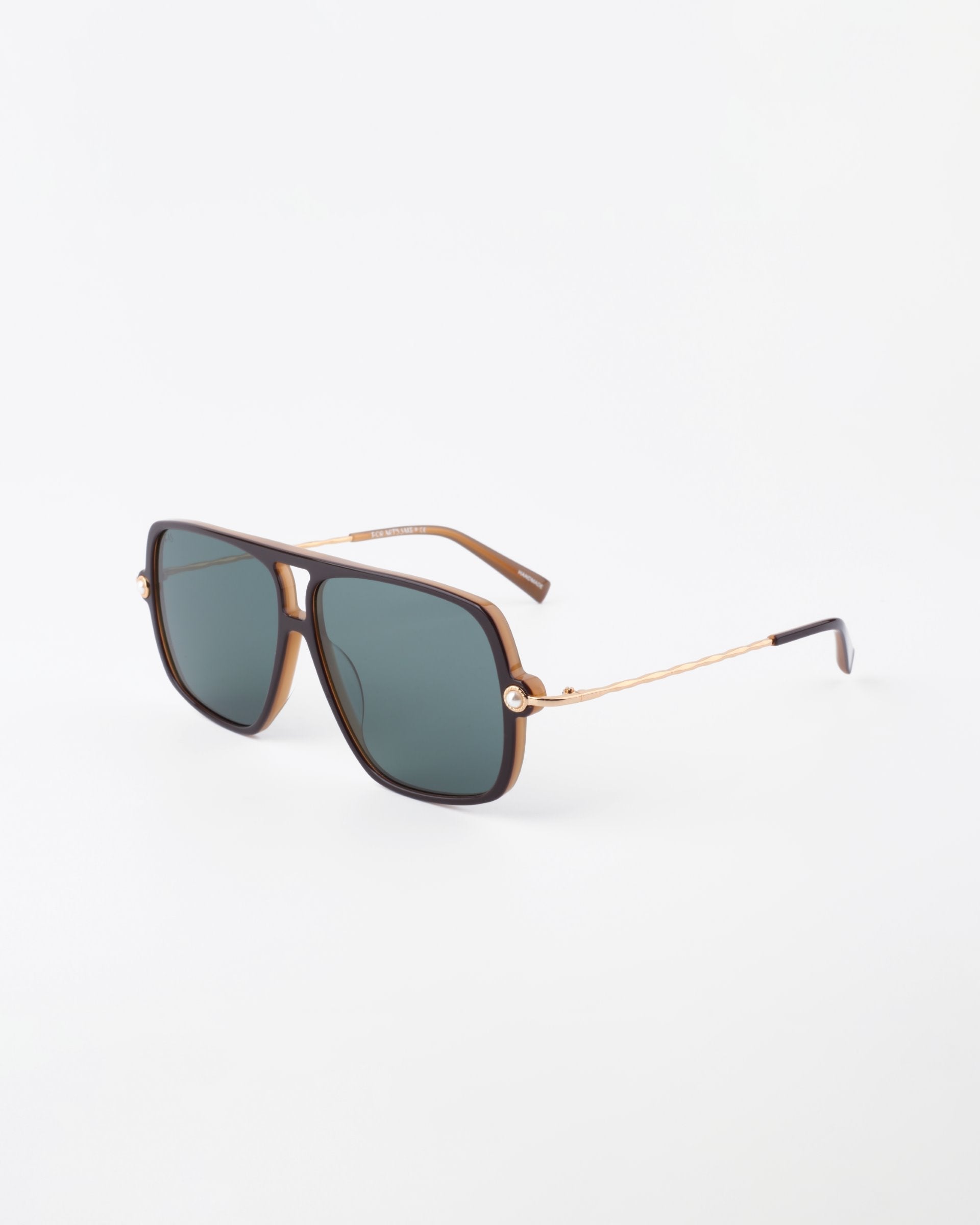 A pair of stylish For Art's Sake® Cinnamon Green sunglasses with a gold frame and dark green-tinted, rectangular lenses. The arms are thin with small hinge details, featuring handmade 18-karat gold-plated elements. The overall design is modern and sleek, poised perfectly against a plain white background.