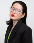 A person with straight dark hair wears the Cleo glasses by For Art's Sake®, a black blazer, and red lipstick, posing confidently against a plain white background. Final sale—no returns accepted.