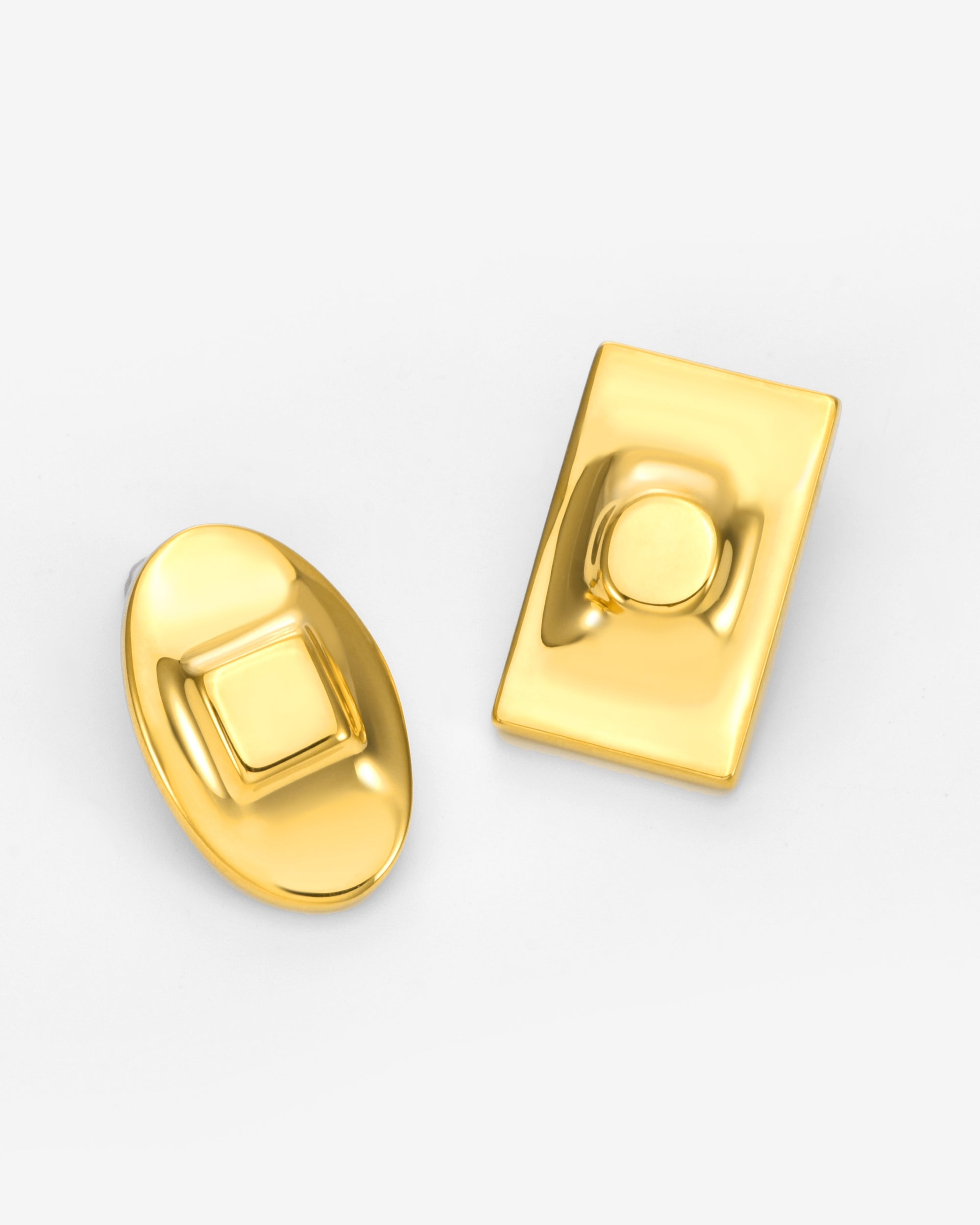 The Geometry Earrings by For Art's Sake®: a shiny gold oval earring with a raised square center and a shiny gold rectangular earring with a raised circular center, both displayed on a white background.