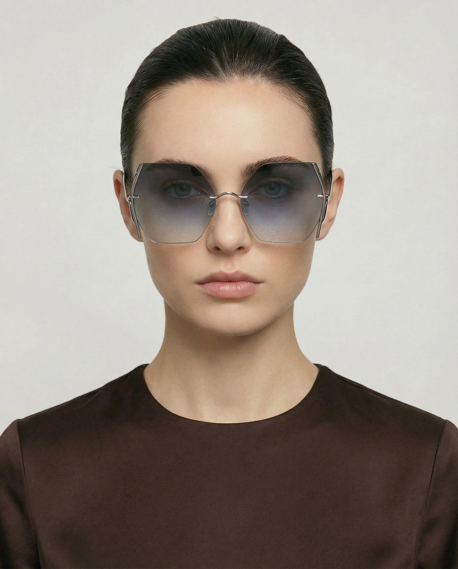 A person with straight dark hair pulled back, wearing For Art's Sake® Generation large geometric gradient sunglasses for UV protection and a dark brown top, faces forward against a plain light background.