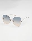 For Art's Sake® Starlight sunglasses feature gradient blue-to-clear lenses, slim gold arms, UV protection, and a chic rimless design, displayed on a white background.