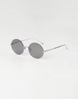 The For Art's Sake® Skyline-Grey sunglasses feature thin silver metal frames and dark tinted lenses, shown next to minimalist earrings on a plain white background.
