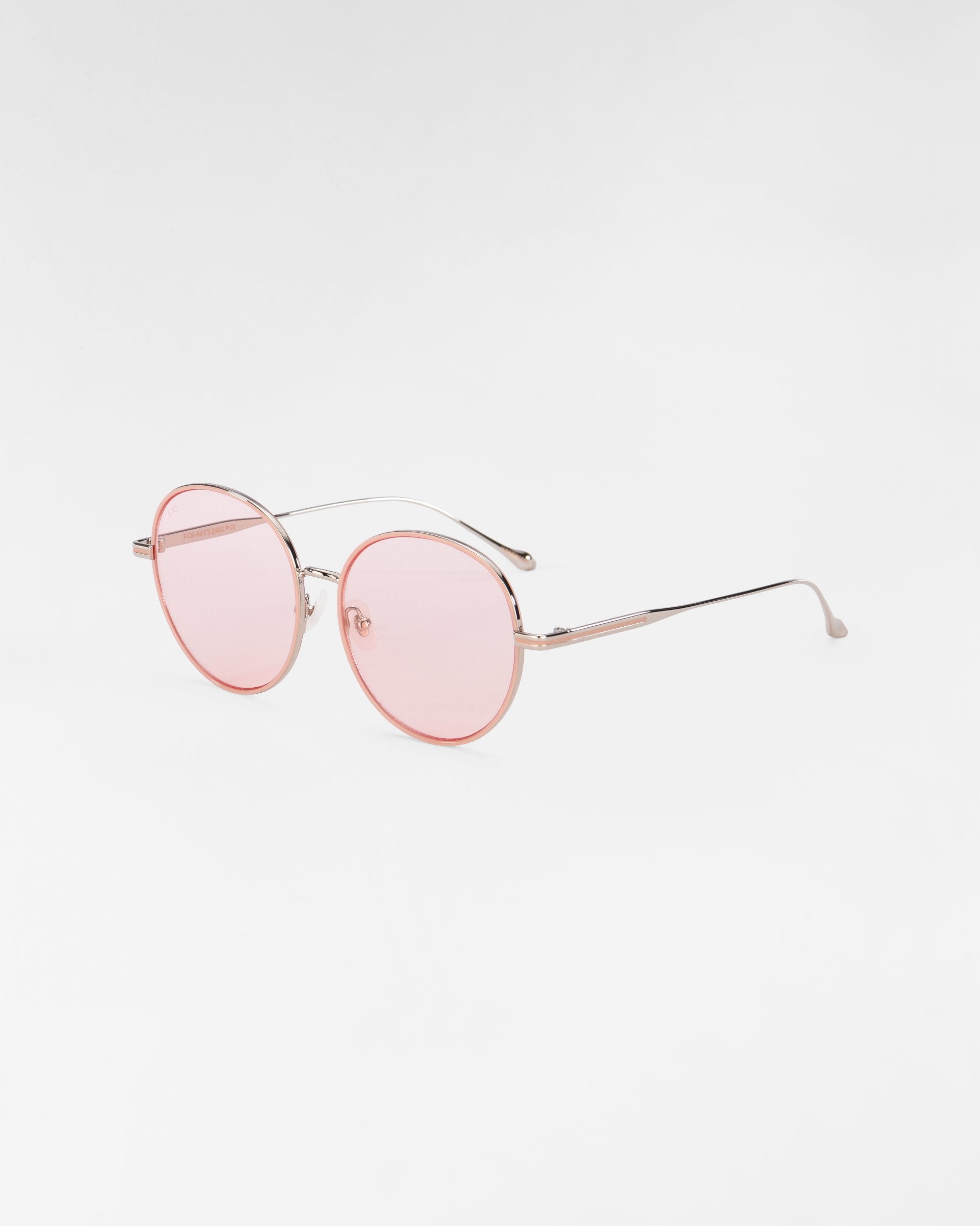 A pair of round, thin-framed For Art's Sake® Lemon sunglasses with pink-tinted lenses and metal temples. The clear nose pads are complemented by hand-painted enamel details. The frame is delicate and minimalistic, set against a plain white background.