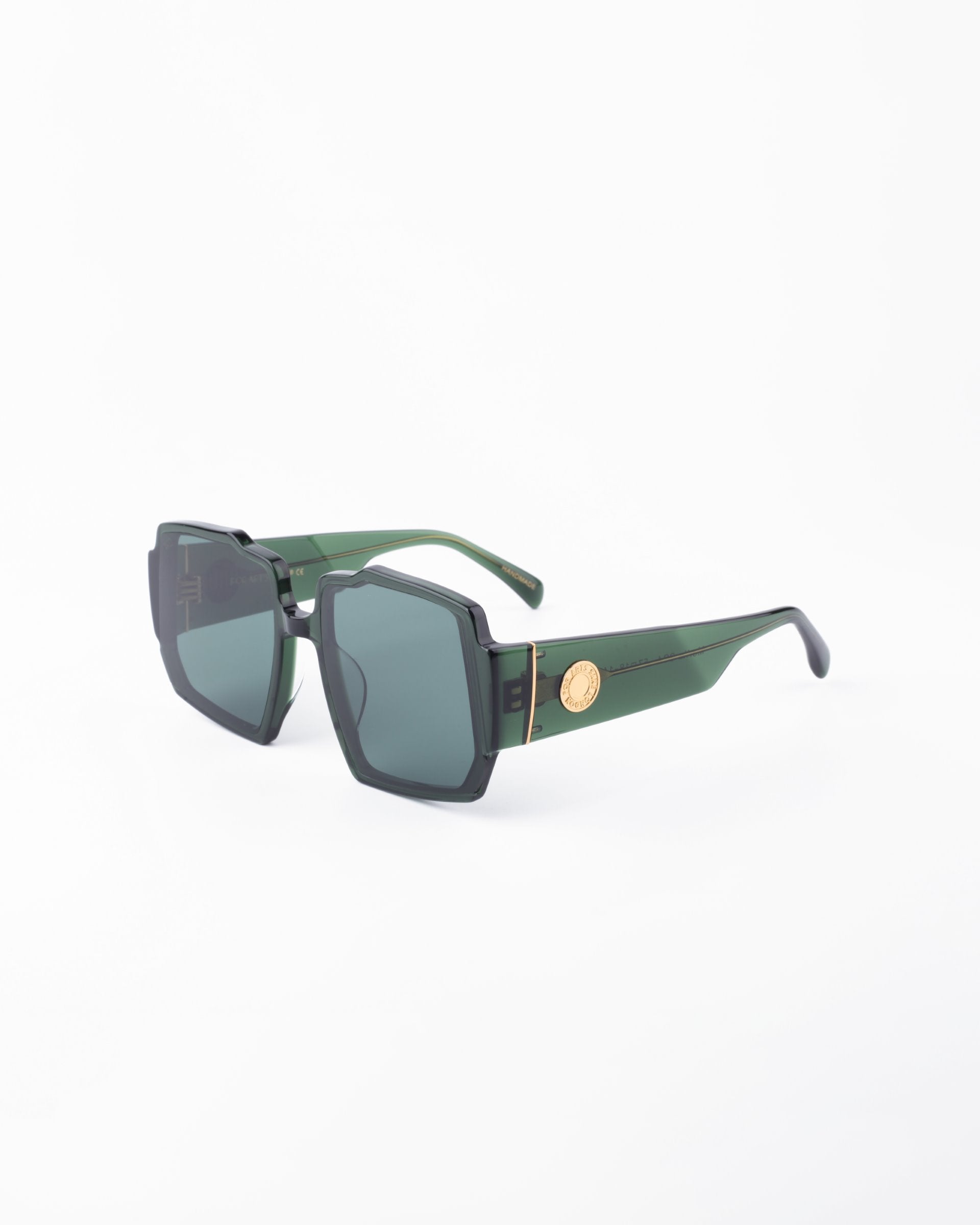 A pair of stylish sunglasses showcasing a chunky acetate frame with green hues, black UV-protected lenses, and gold-tone accents on the temples, photographed against a plain white background. The design features geometric details around the lenses. These are the Moritz by For Art's Sake®.
