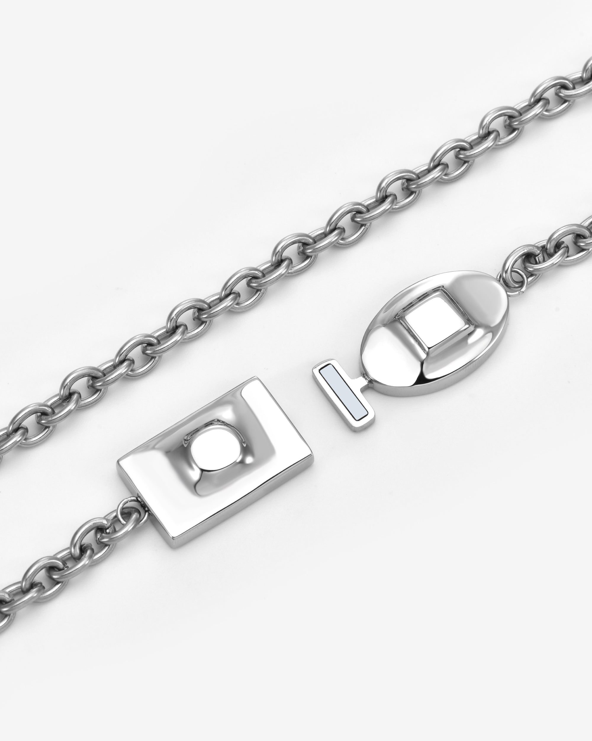 A close-up of The Geometry Necklace by For Art's Sake® showcases its silver chain and distinctive geometric toggle clasp—rectangular and oval links—an elegant piece of modern jewelry set on a white background.
