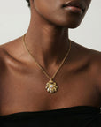 A woman models The Shell Pendant by For Art’s Sake®—a gold sculptural sea shell necklace with a central freshwater pearl—styled with a black strapless top against a neutral backdrop to highlight its elegance.