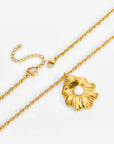 The Shell Pendant Bracelet by For Art's Sake® features a textured gold flower-shaped charm with a central white pearl, an adjustable chain, lobster clasp, and circular charm, shown on a light background.