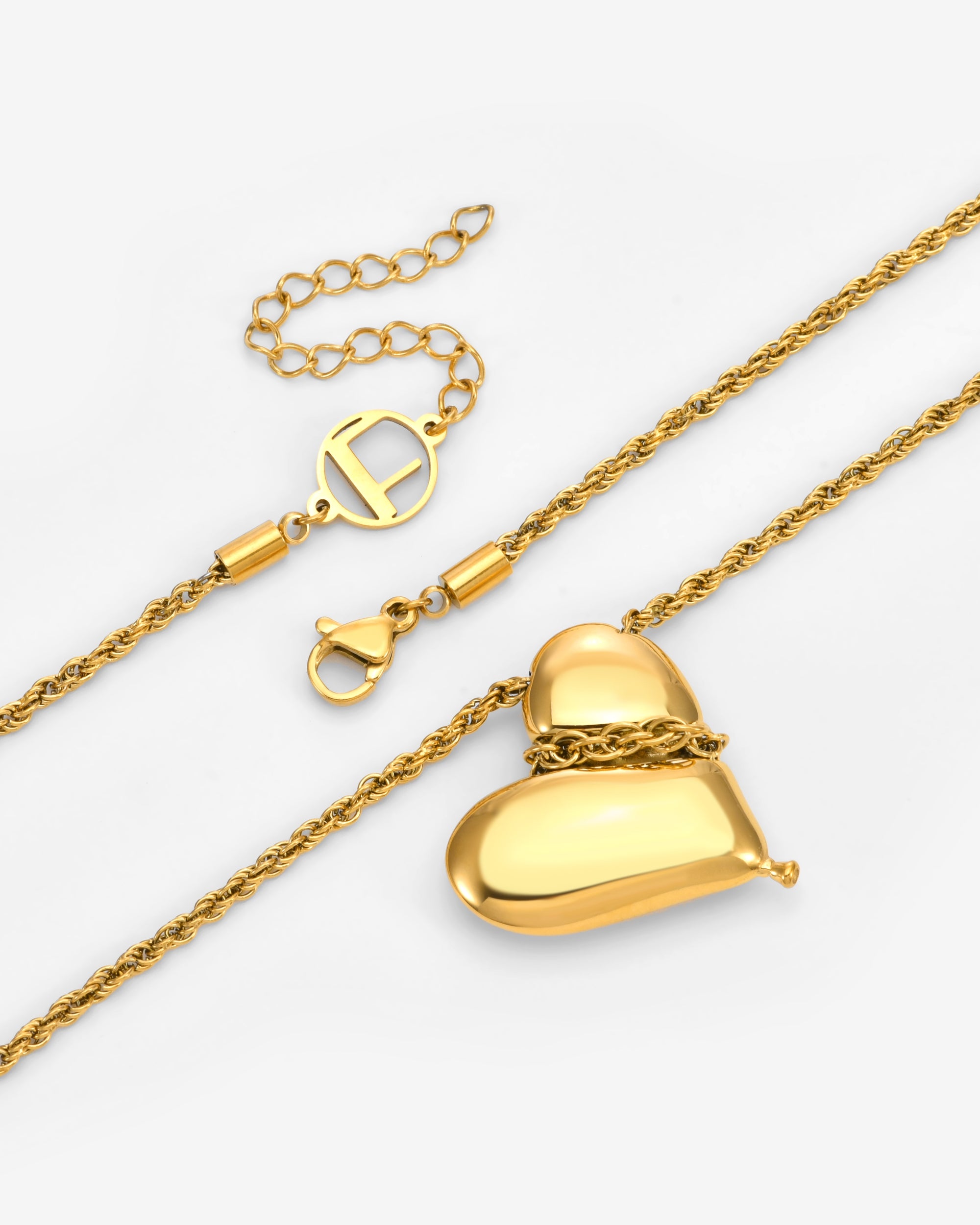 The Puffy Heart Bracelet by For Art's Sake® features a shiny, heart-shaped pendant, an adjustable clasp with an extension chain, and a decorative circular charm. Displayed on a light background.