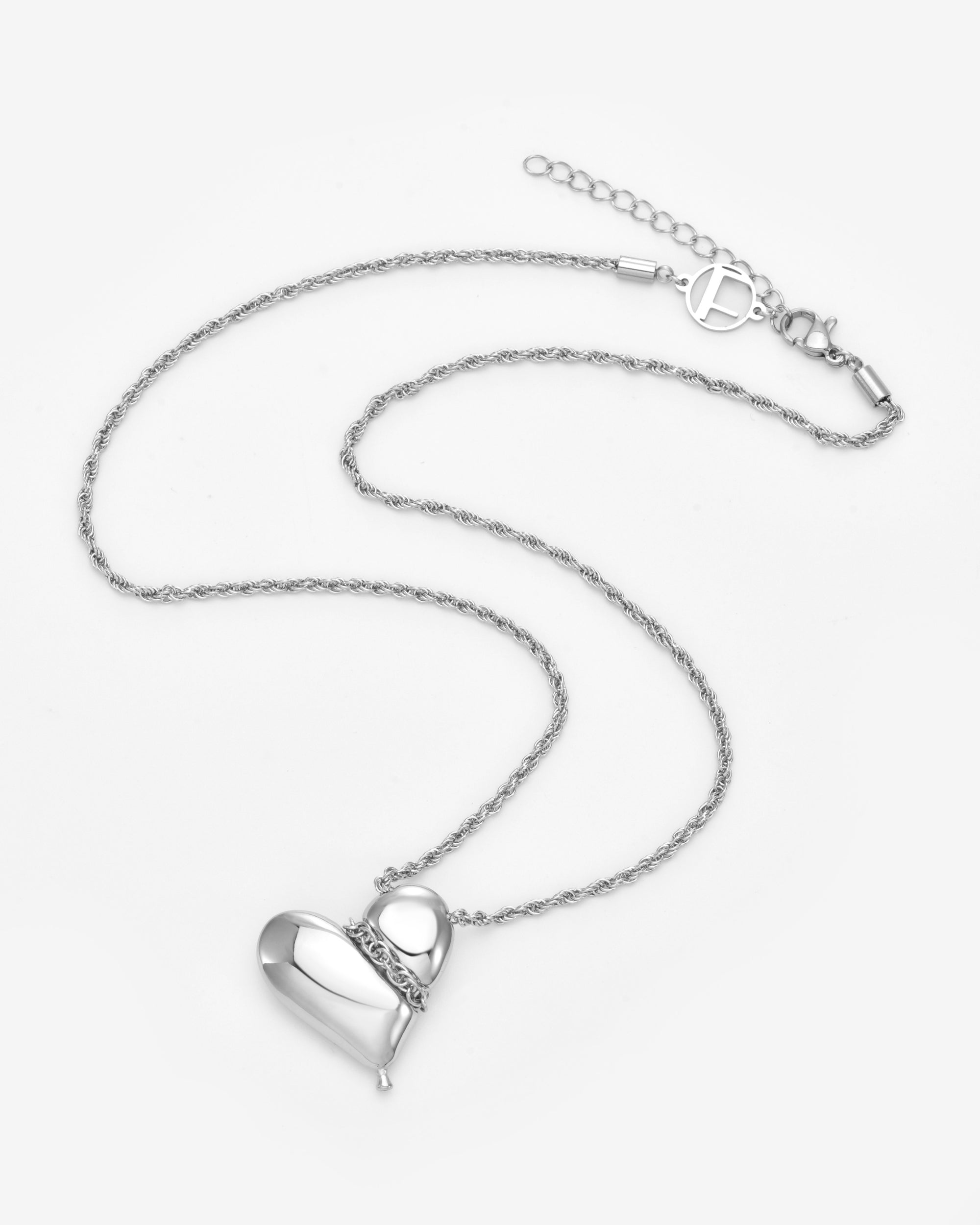 The Puffy Heart Pendant by For Art's Sake® is a silver necklace with a smooth puffed heart charm, a small decorative loop, and a textured chain with toggle clasp, shown against a plain light background.