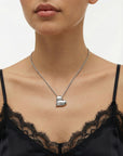 A woman wears For Art's Sake® The Puffy Heart Pendant—a shiny, sculpted silver heart—on a chain, paired with a black lace-trimmed camisole. The image is cropped to her neck, shoulders, and upper chest.