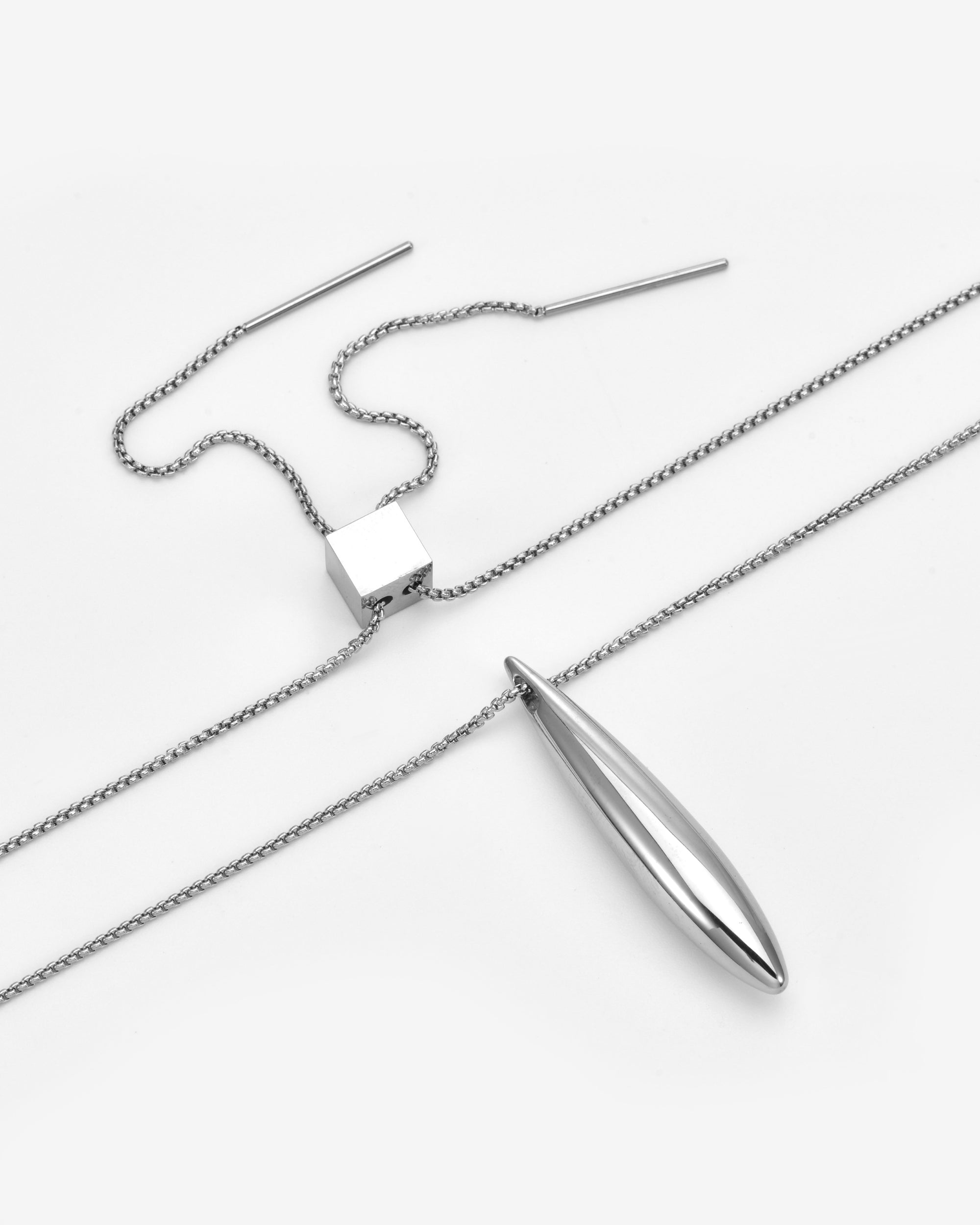 The Droplets Pendant Necklace by For Art's Sake® is a minimalist silver piece featuring a modern metal droplet on a delicate chain, paired with geometric cube and slender bar accents, displayed on a white background.