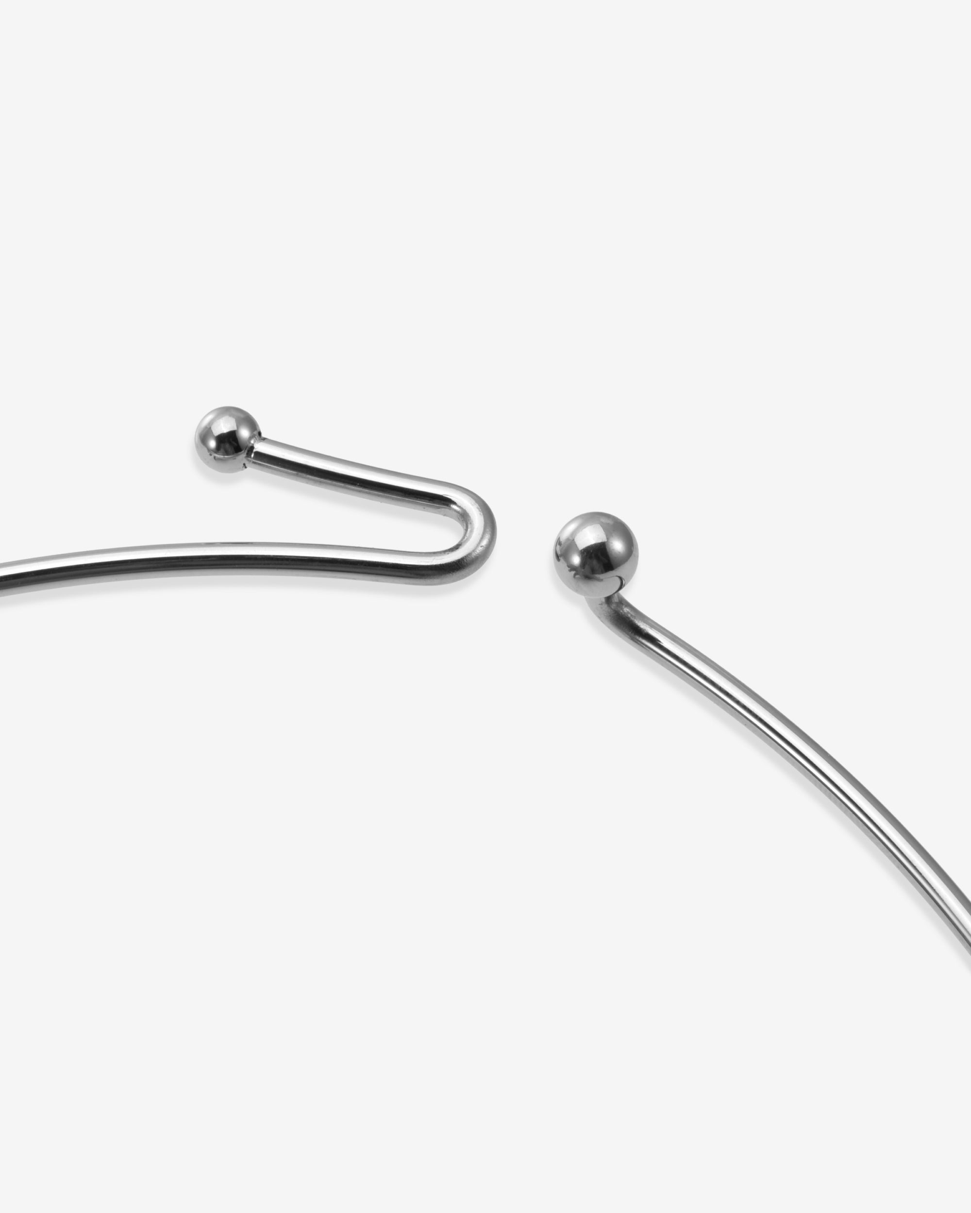 A close-up of The Rose Choker by For Art’s Sake® shows two ends with small spherical beads, highlighting its sleek, open-ended silver metal design—an elegant piece of modern jewelry against a plain white background.