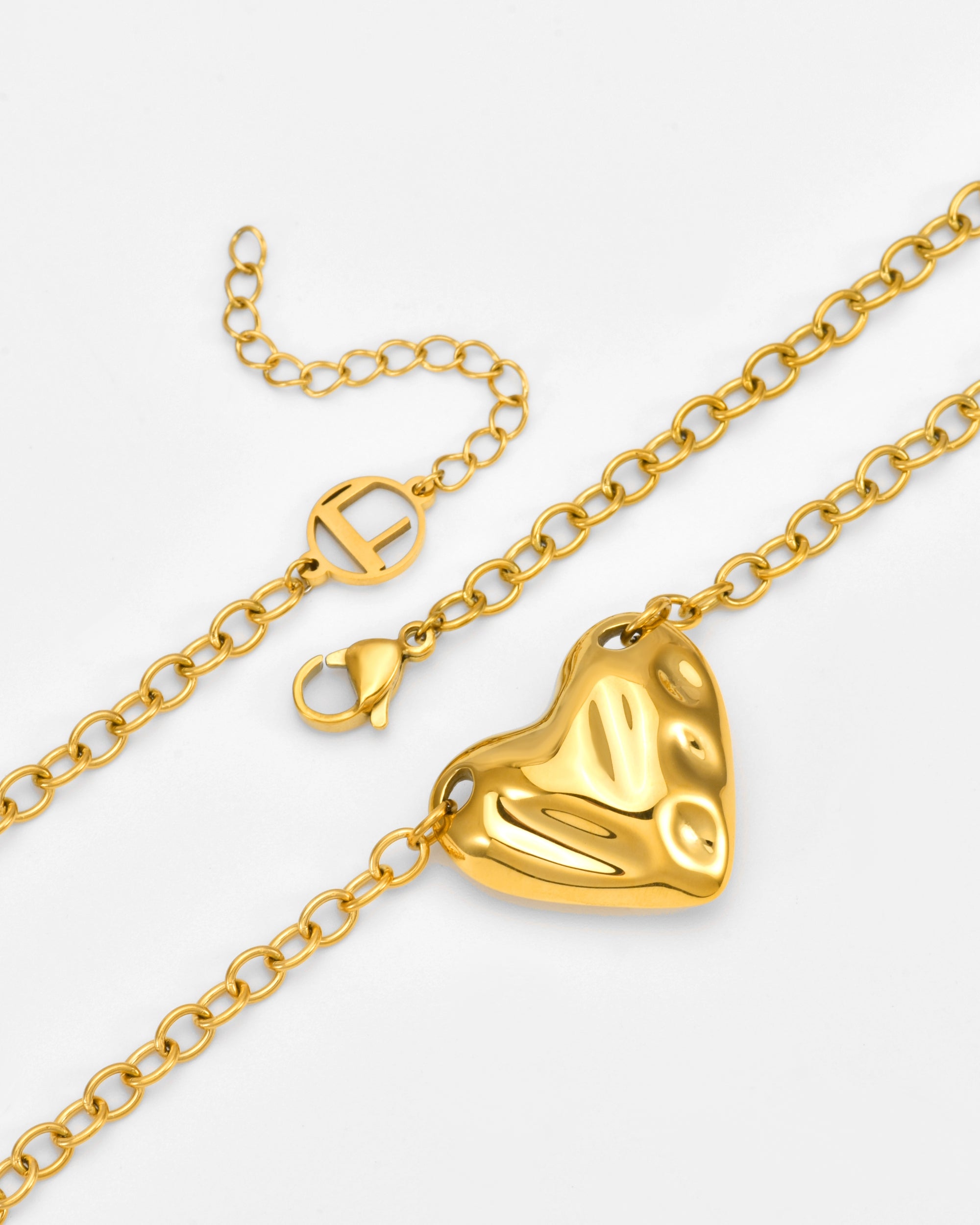 The Sculpted Heart Necklace by For Art's Sake® features a gold chain with a textured, abstract heart-shaped pendant and lobster clasp, plus an extension chain adorned with a small circular cut-out charm.