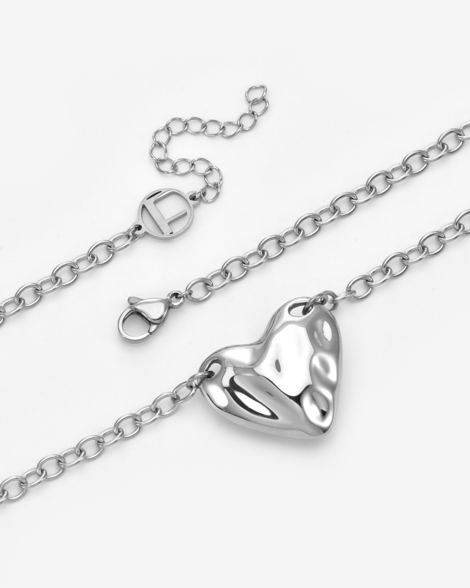 A close-up of For Art's Sake® The Sculpted Heart Necklace, featuring a delicate chain, shiny sculptural heart pendant, and lobster clasp, set against a plain white background.