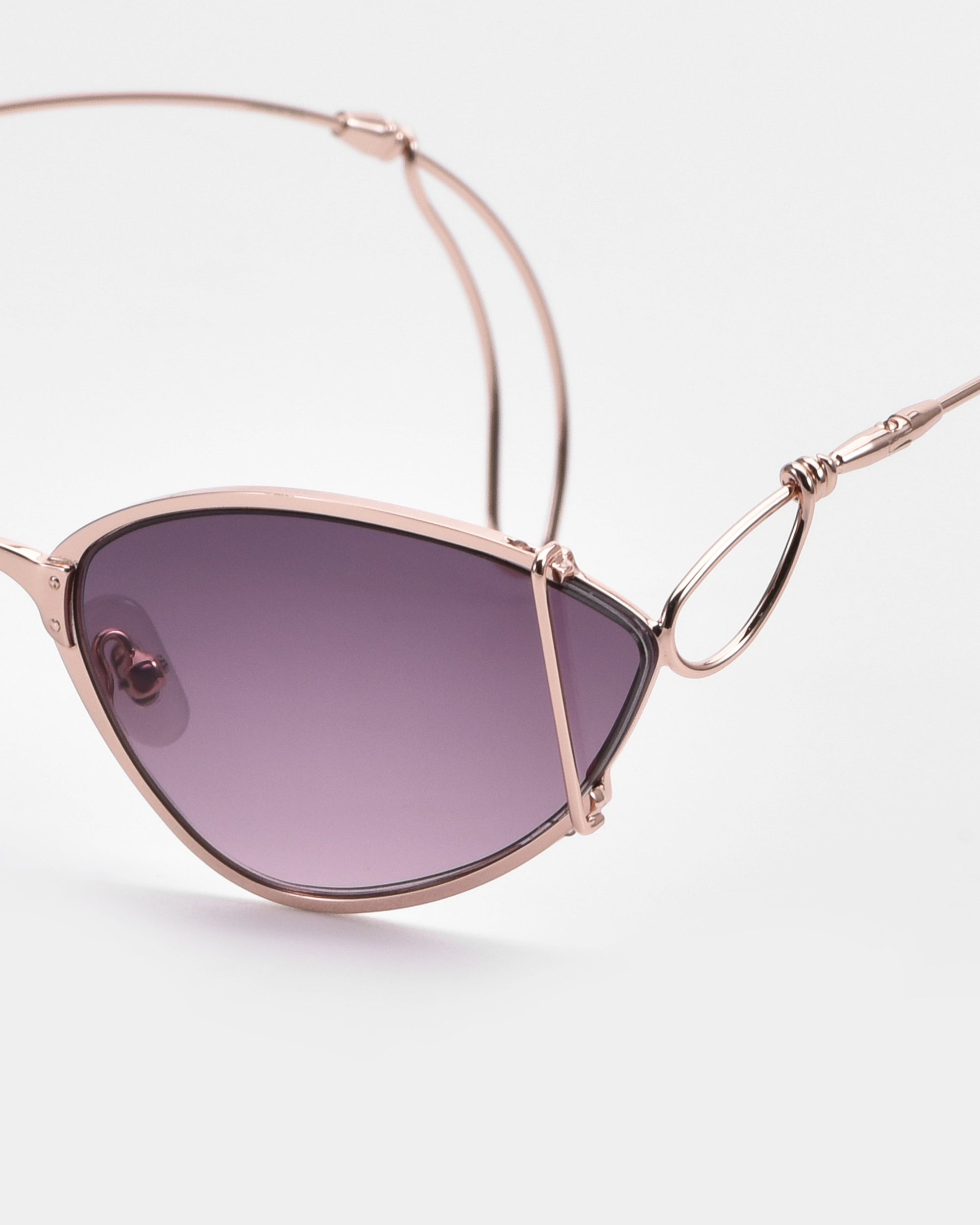 Close-up of For Art&#39;s Sake® Ornate sunglasses with almond-shaped lenses, an artistic wire design, edgy rose gold metal frame, and dark purple tints, set against a plain white background.