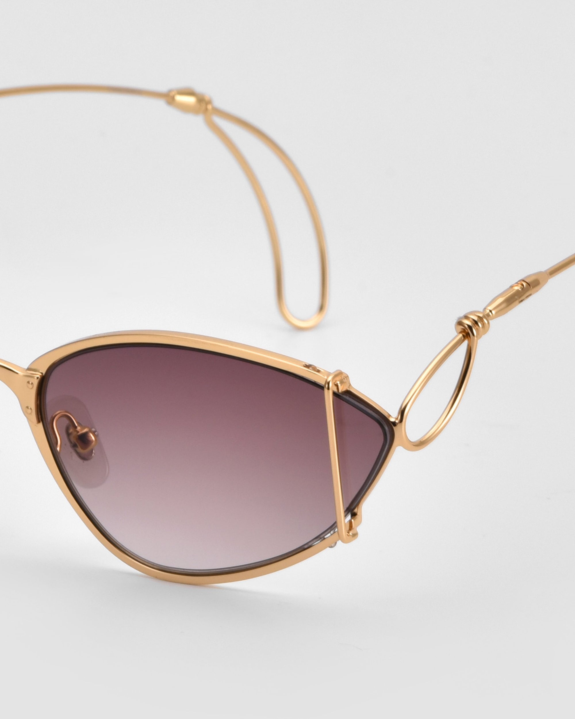 A close-up of For Art&#39;s Sake® Ornate sunglasses, featuring stylish gold almond-shaped frames, dark gradient lenses, and distinctive wire-detailed arms against a plain light background.