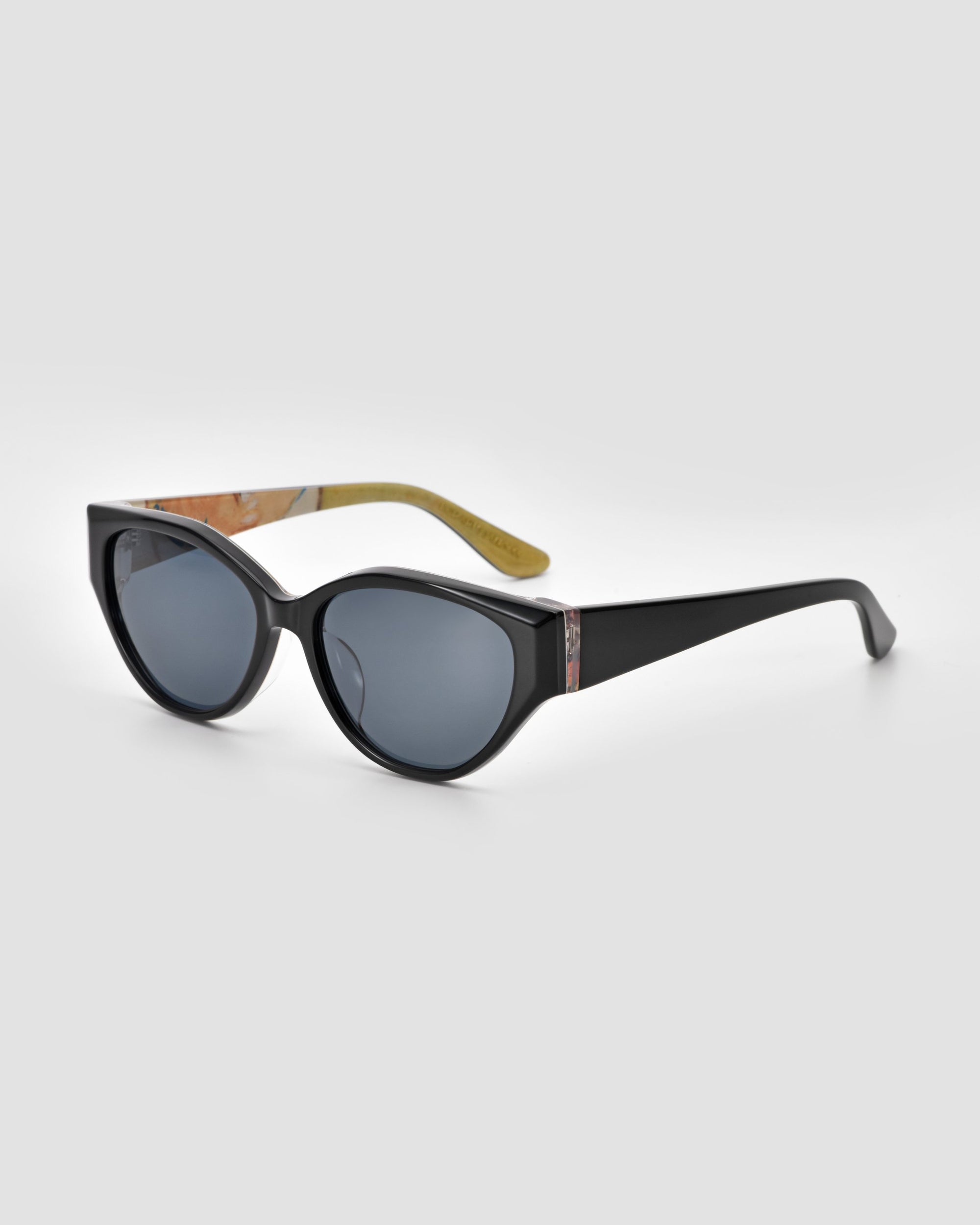 The For Art's Sake® Vincent Van Gogh sunglasses feature black cat-eye frames, dark lenses, a decorative detail, and a beige patterned inner arm—perfect collectible eyewear, displayed on a light gray background.