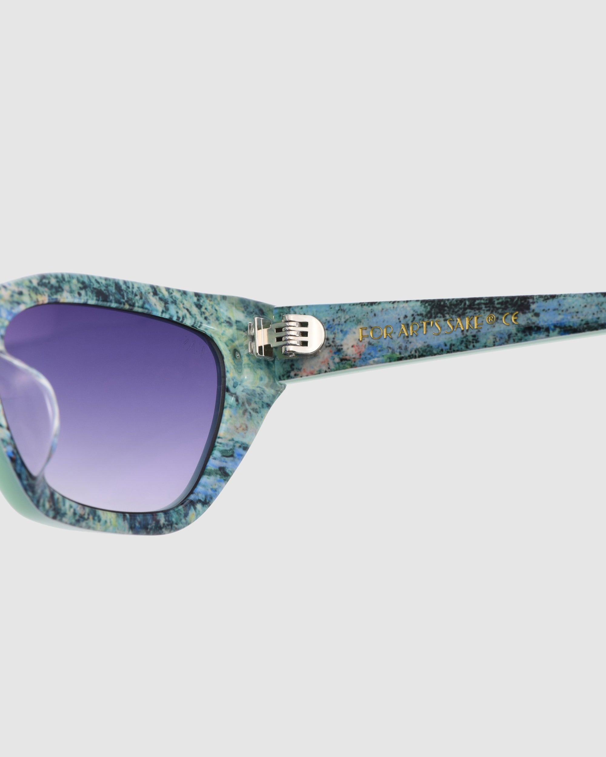 Close-up of Claude Monet (Limited Edition) cat-eye sunglasses by For Art&#39;s Sake®, featuring a blue and green marbled frame, purple tinted lenses, and gold text on the arm.