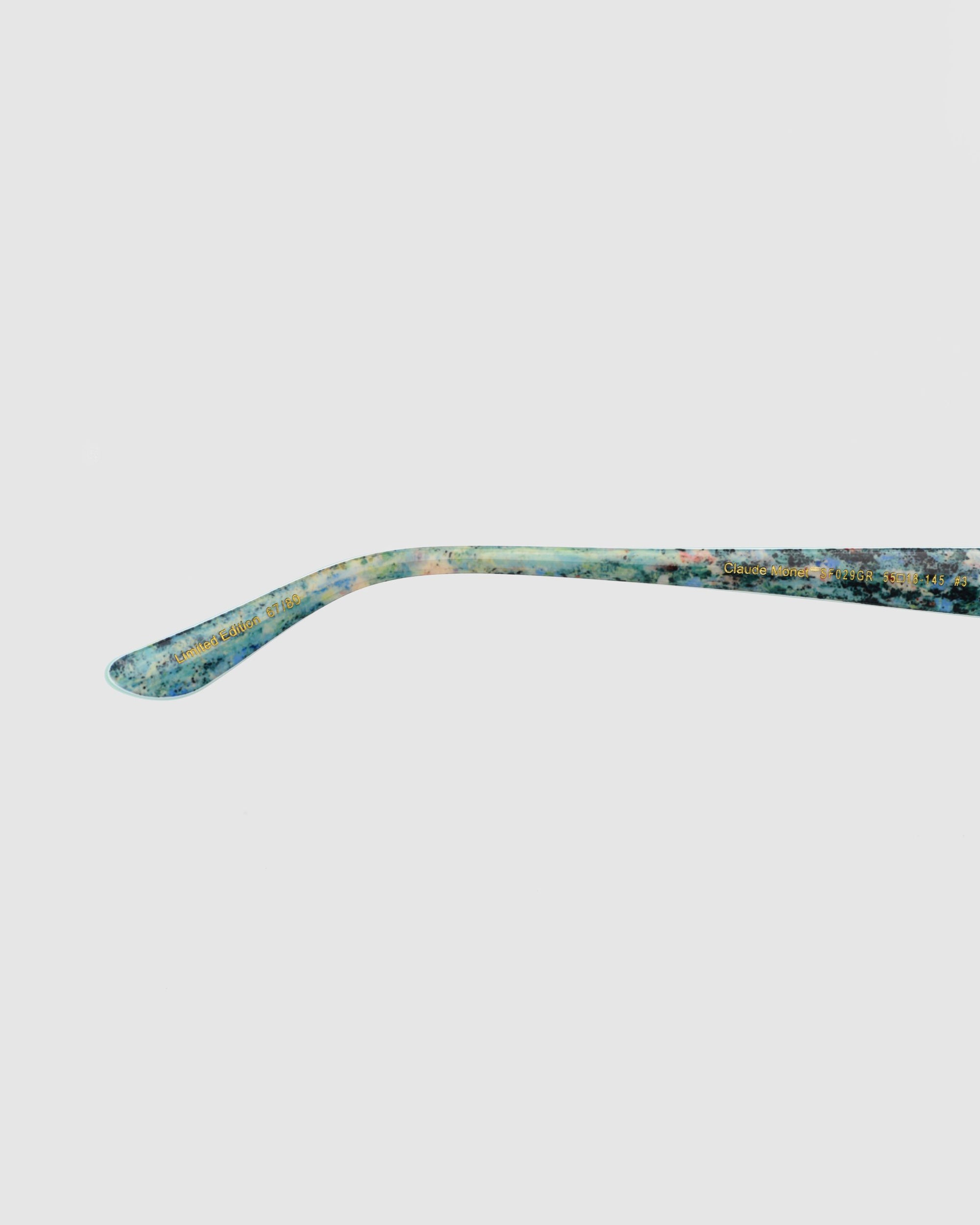 The Claude Monet (Limited Edition) by For Art&#39;s Sake® is a thin, slightly curved metallic object with a greenish-blue patina, evoking vintage sunglasses style, displayed on a plain white background.