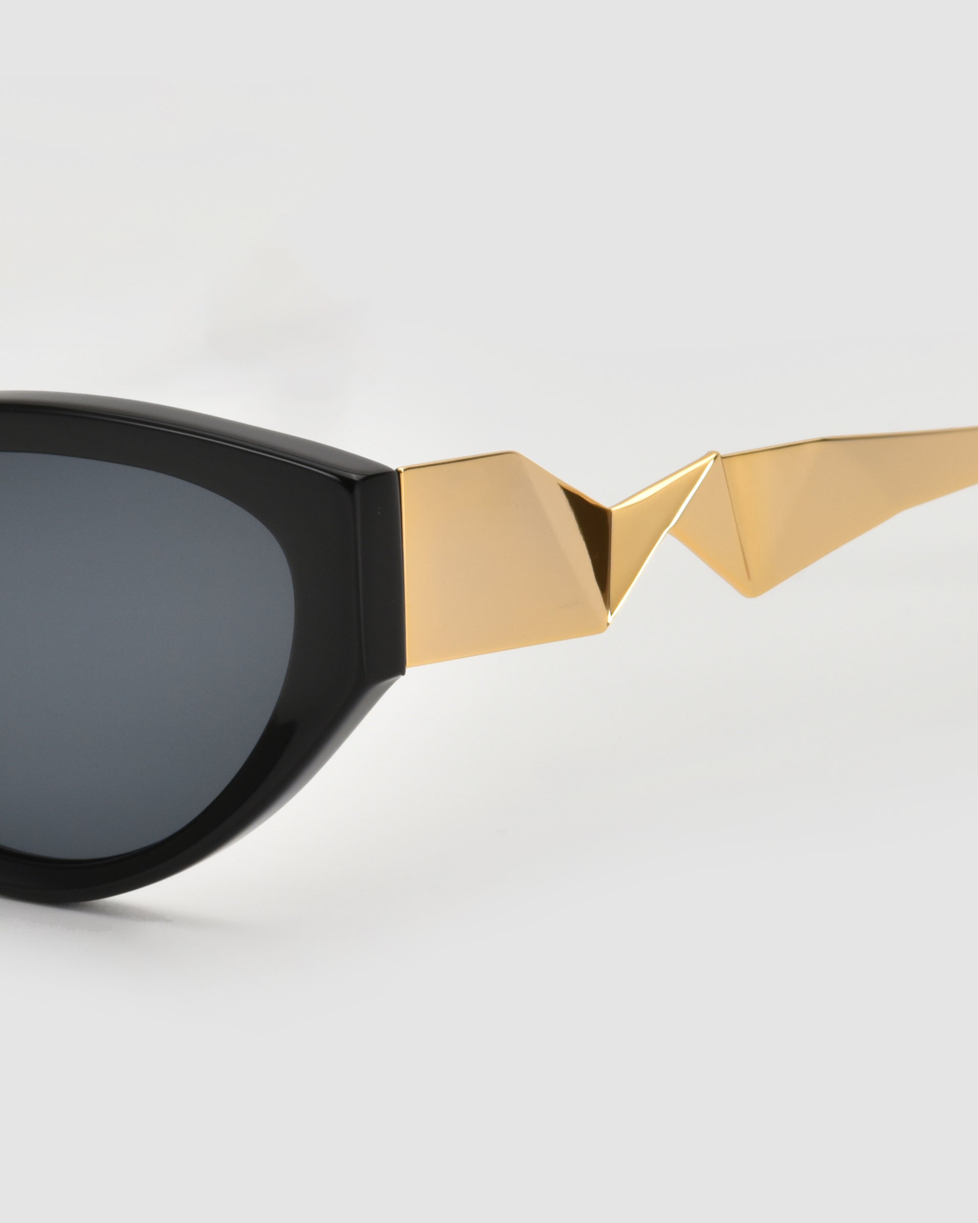 Close-up of For Art&#39;s Sake® Unfold sunglasses featuring a unique gold geometric design and pleated temples, set against a plain light gray background.