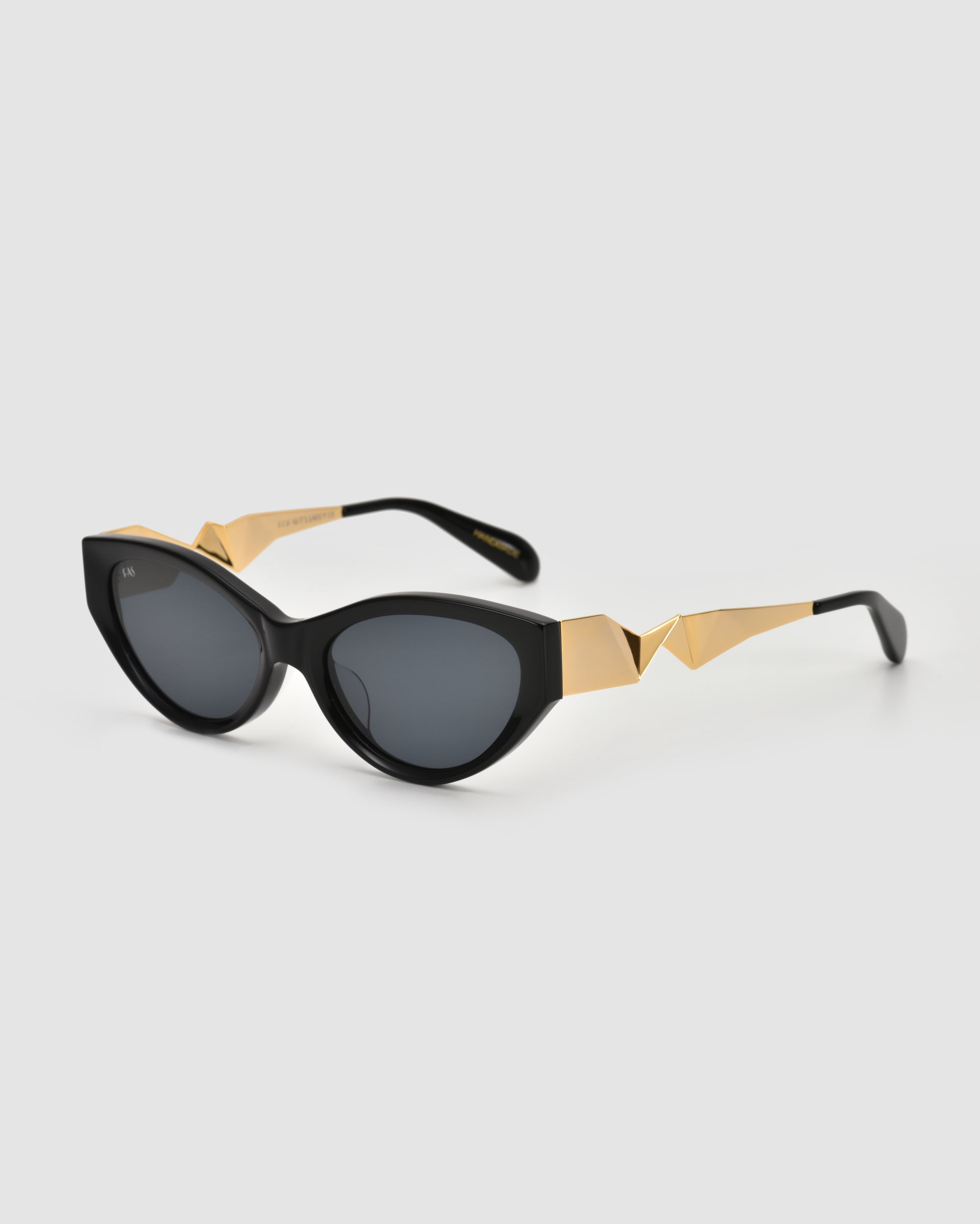 The Unfold sunglasses by For Art’s Sake® feature black sculptural frames, dark lenses, and geometric gold arms, shown on a plain light background.