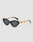 The Unfold sunglasses by For Art’s Sake® feature black sculptural frames, dark lenses, and geometric gold arms, shown on a plain light background.