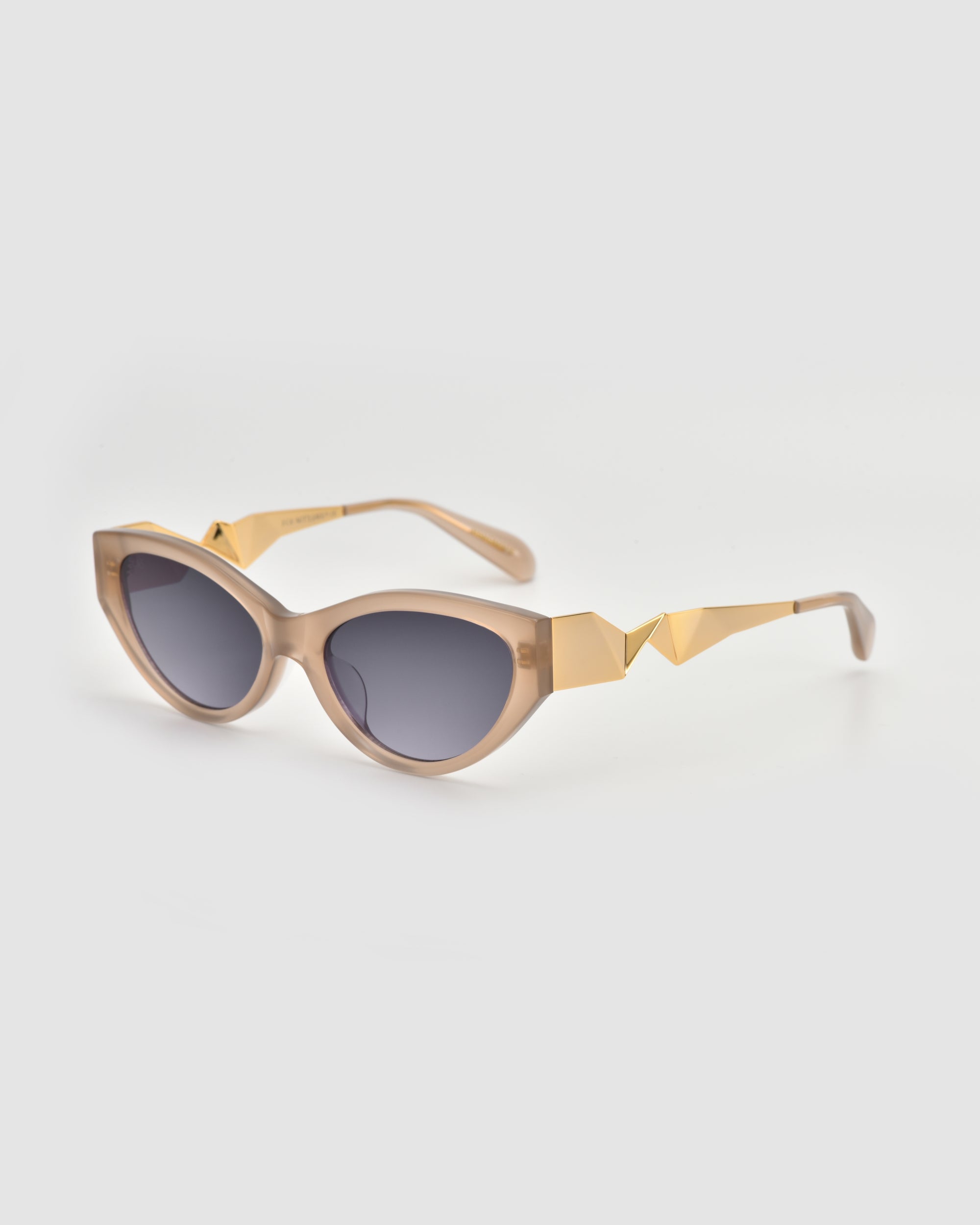 Unfold by For Art's Sake®: Beige cat-eye sunglasses with dark tinted lenses and gold geometric accents on the arms. Their sculptural design offers a modern, stylish touch against a simple light gray background.
