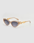 Unfold by For Art's Sake®: Beige cat-eye sunglasses with dark tinted lenses and gold geometric accents on the arms. Their sculptural design offers a modern, stylish touch against a simple light gray background.
