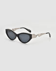 For Art’s Sake® Unfold black oval cat-eye sunglasses feature dark lenses and striking angular silver arms, making a bold geometric statement on a plain light background.