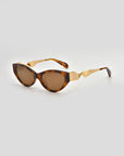 For Art's Sake® Unfold sunglasses: tortoiseshell cat-eye frames with brown lenses and gold geometric arm detailing, showcased as striking geometric eyewear on a light gray background.