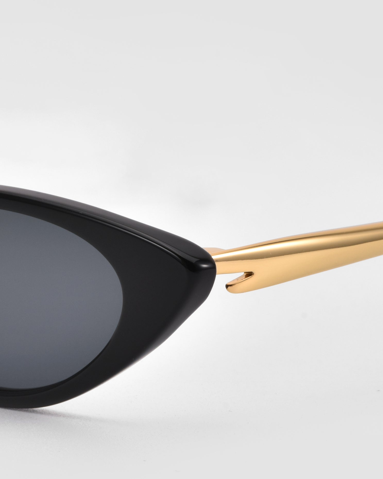 Close-up of the left side of For Art’s Sake® Slash cat-eye sunglasses, featuring a black frame and gold arm, set against a plain light gray background.