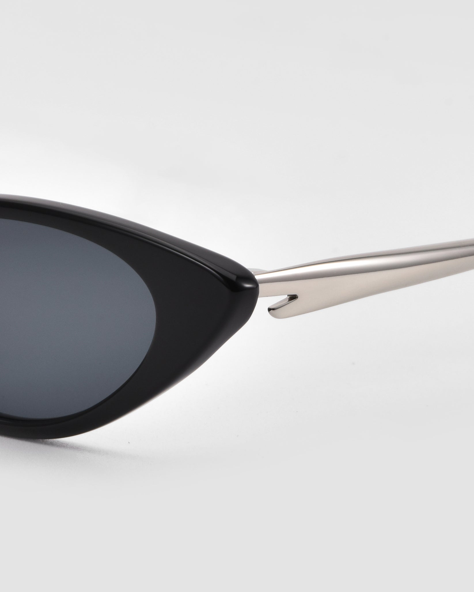 Close-up of the For Art&#39;s Sake® Slash cat-eye sunglasses, inspired by Lucio Fontana, featuring black frames, dark lenses, and silver metallic arms, set against a plain light background.