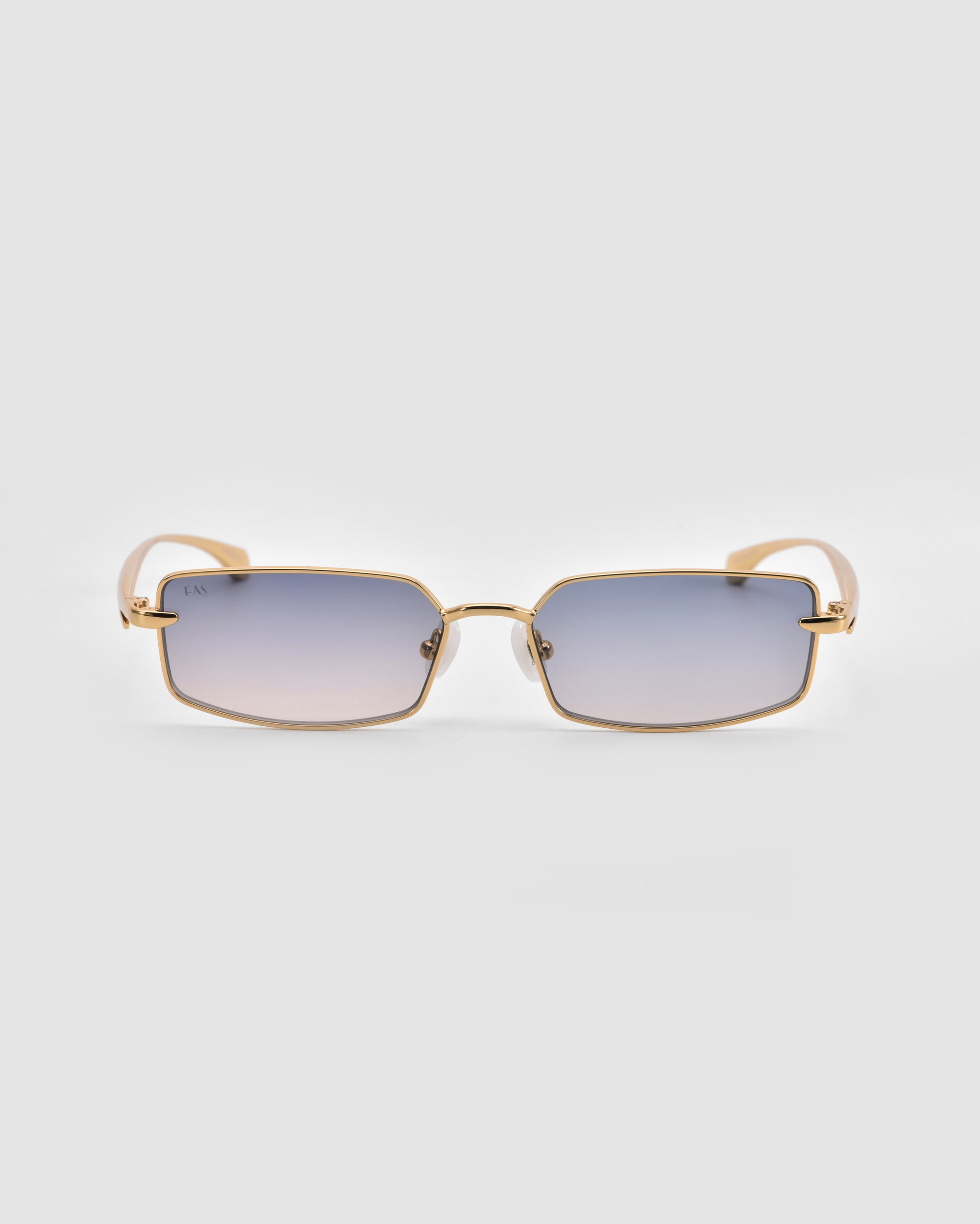 For Art's Sake® Lucio sunglasses feature a sculpted rectangular gold metal frame and gradient lenses fading from blue to clear, shown on a light gray background.