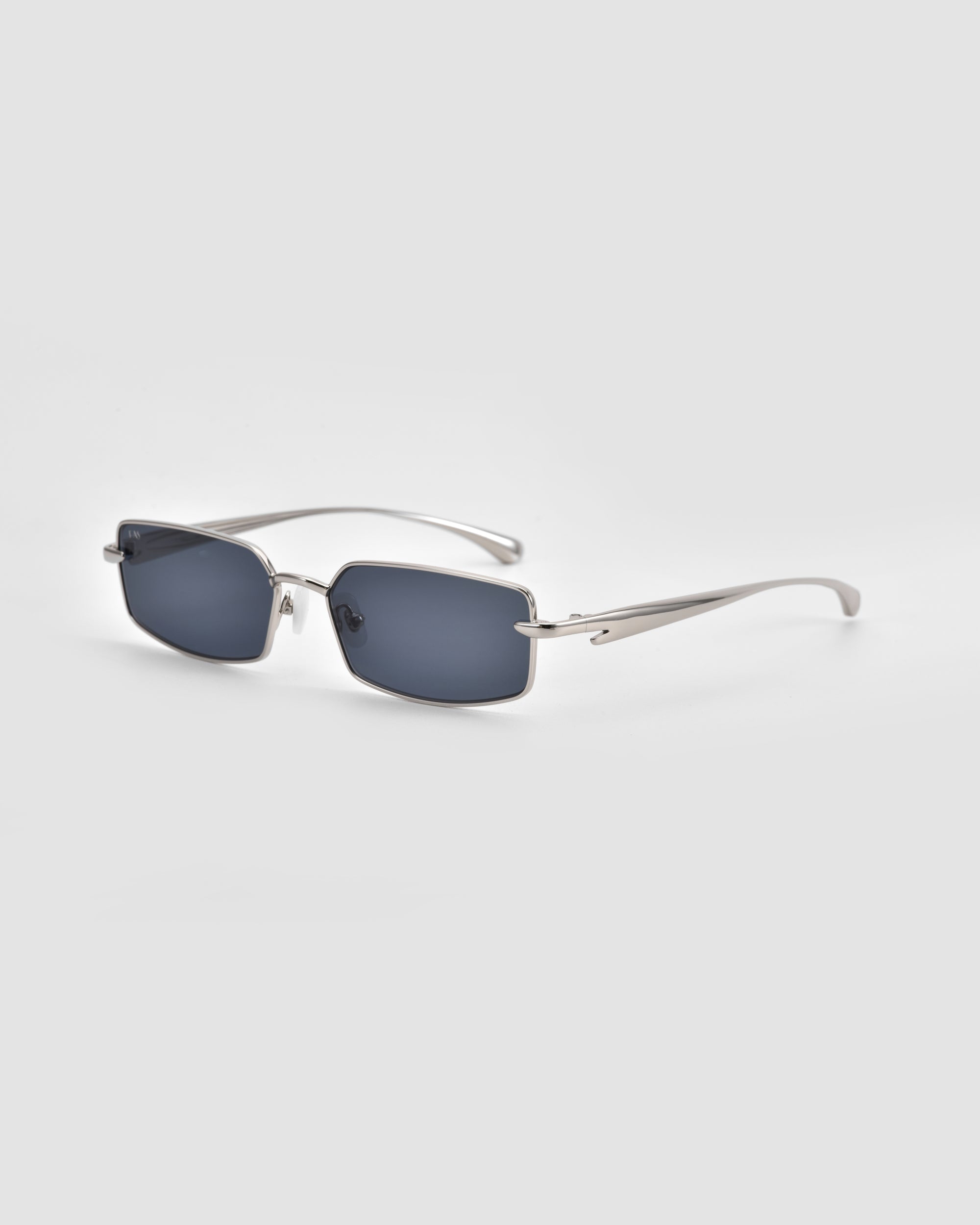 For Art's Sake® Lucio sunglasses feature rectangular silver metal frames with dark tinted lenses, thin slightly curved temples, and a unique 3D swoosh design, displayed on a light gray background.