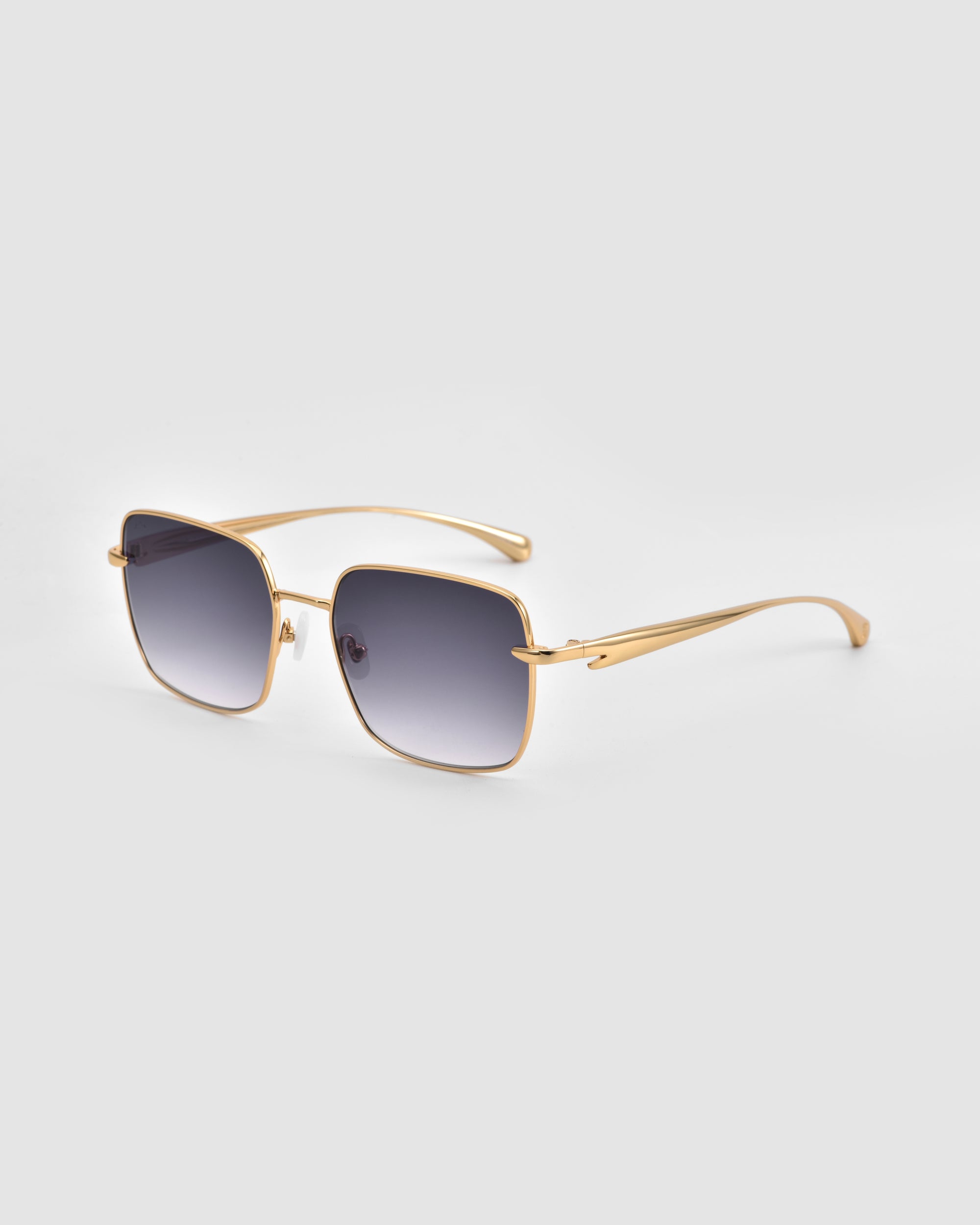 The Edge sunglasses by For Art's Sake® feature gold frames, sculptural details, and dark gradient lenses. Displayed on a light gray background, the image shows the front and side arm for a stylish look.
