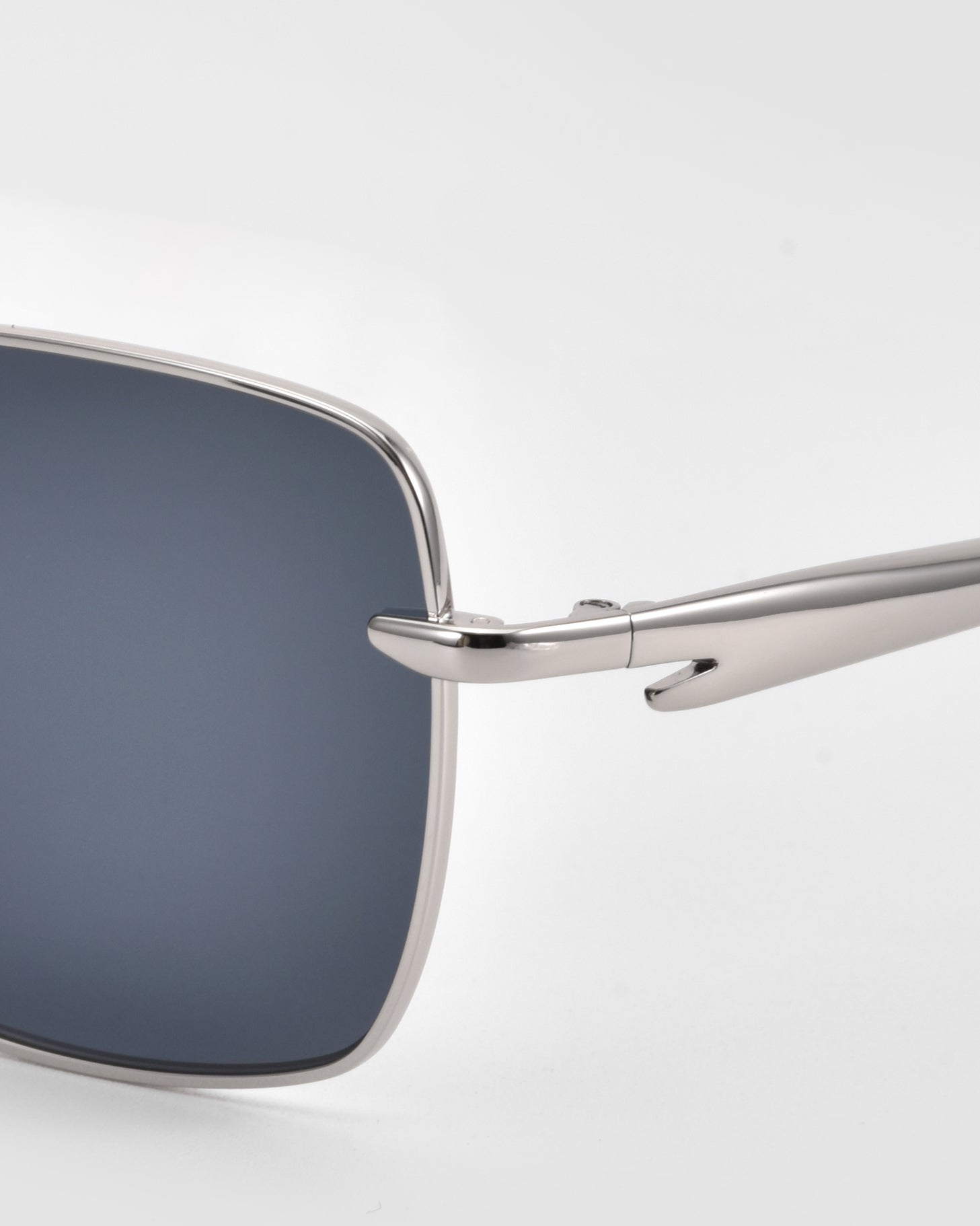 Close-up of the left lens and arm of For Art&#39;s Sake® Edge sunglasses, featuring a sleek square silhouette with silver metal frames and dark lenses against a plain light background.