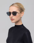 A woman with blonde hair tied back models For Art's Sake® Spark rimless cat-eye sunglasses and a high-neck black top against a plain light gray background.