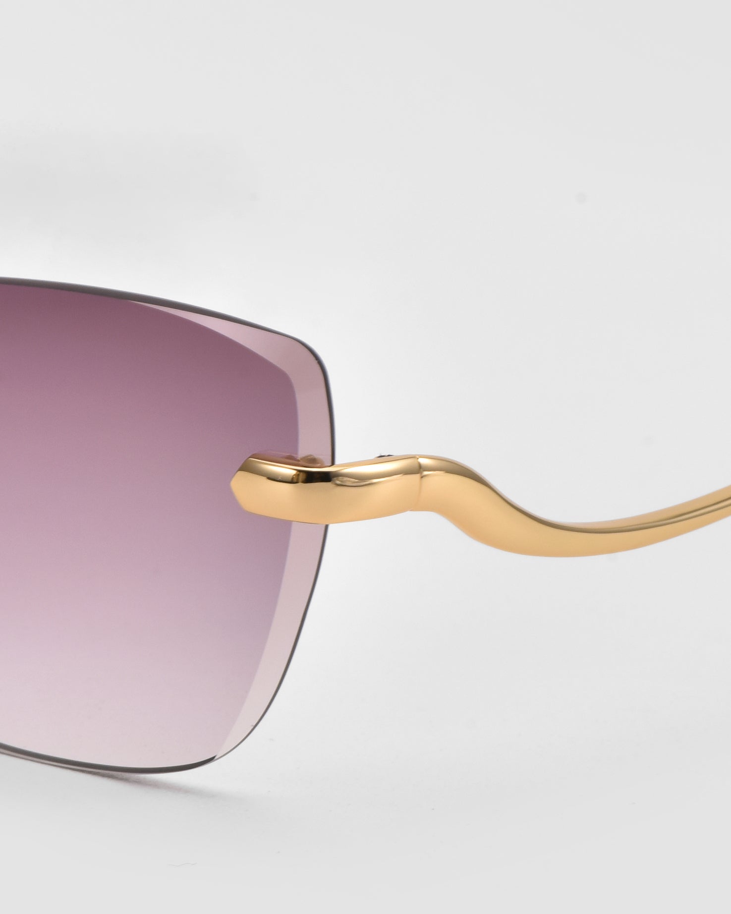 Close-up of For Art&#39;s Sake® Spark rimless cat-eye sunglasses featuring a gold arm and a gradient lens fading from purple to clear, set against a plain light gray background.