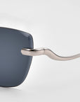 Close-up of the For Art's Sake® Spark sunglasses, highlighting the dark rectangular lens and metallic curved temple arm against a plain light background.